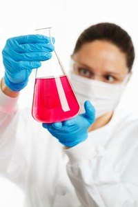 the lab technician looks at the red liquid in the chemical glass bottle